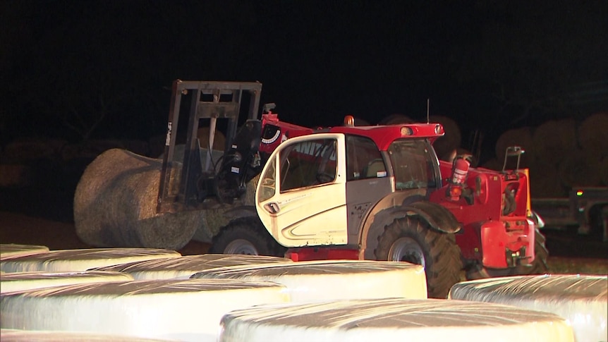 A tractor with round hay bales loaded onto its forks, it is night time