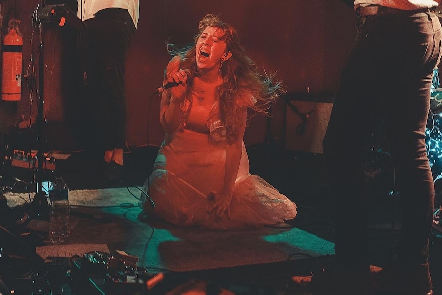 A woman sitting on a stage while singing passionately. 