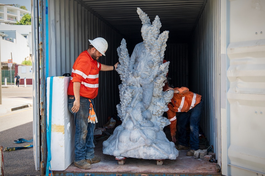 Two men in work wear move a large concrete sculpture from the back of a shipping container
