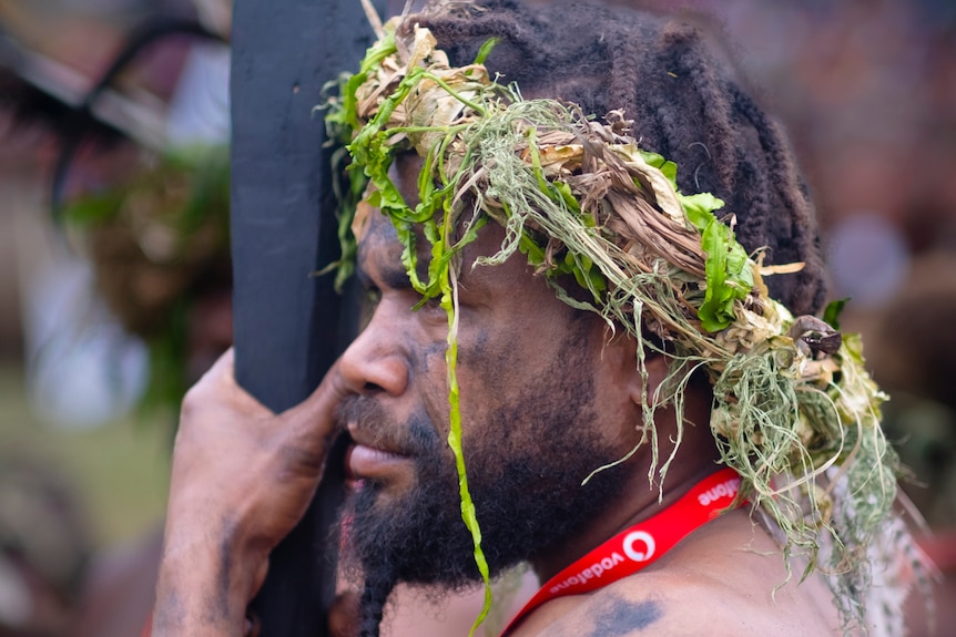 A Melanesian cultural performer holds a black club wearing woven grass headpiece
