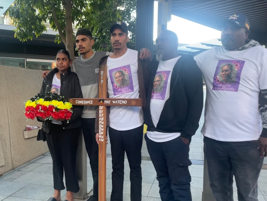 Four men and a woman pose with a wooden cross with Ms Watcho's name on it.