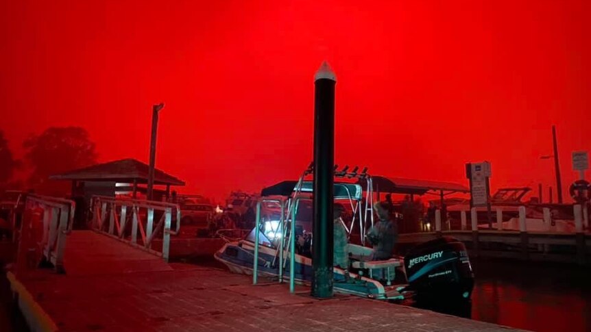 A boat in a dock against a bright-red sky.