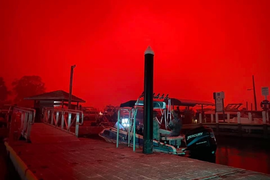 A boat in a dock against a bright-red sky.