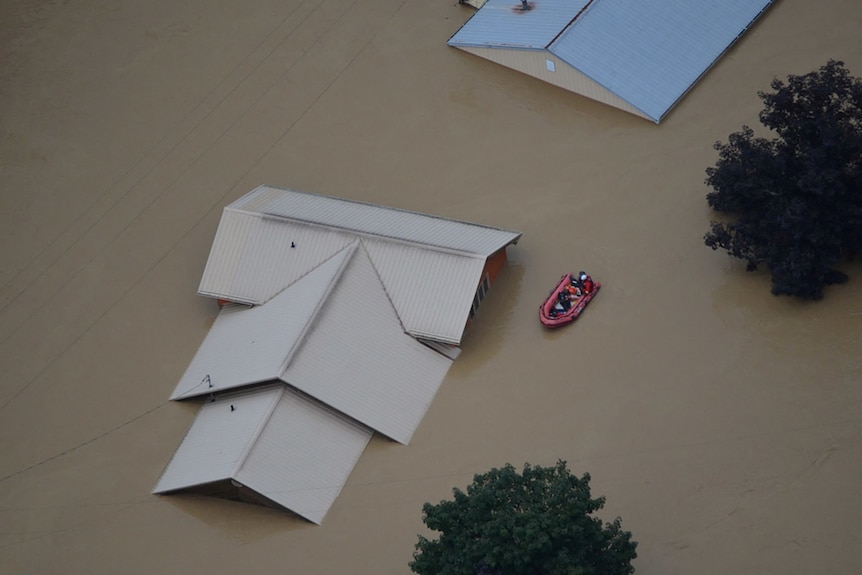 An image taken from the air shows just the roof of a house above brown flood water
