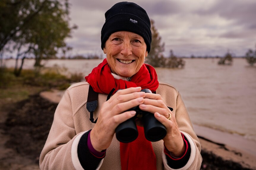 a woman with binoculars with water behind