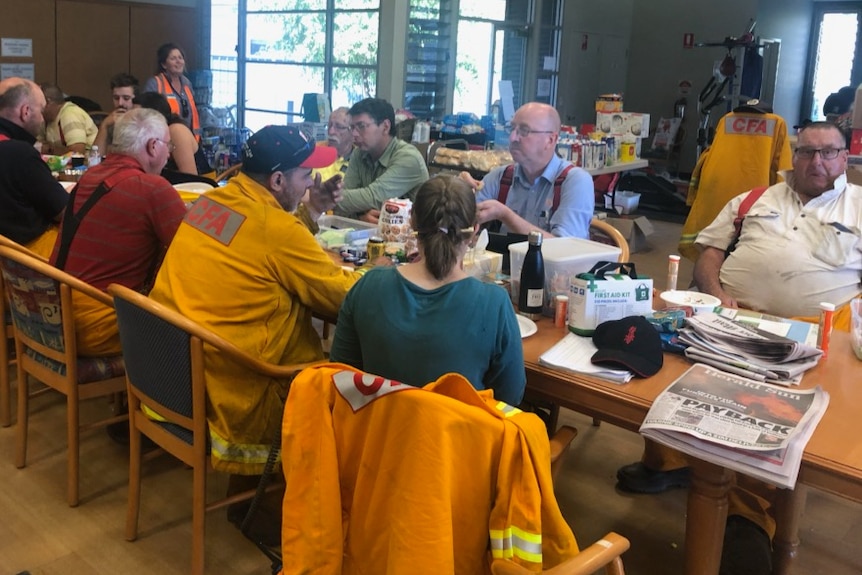 Members of the CFA and locals gather around a table eating a meal inside the Walwa Bush Nursing Centre during the bushfires.