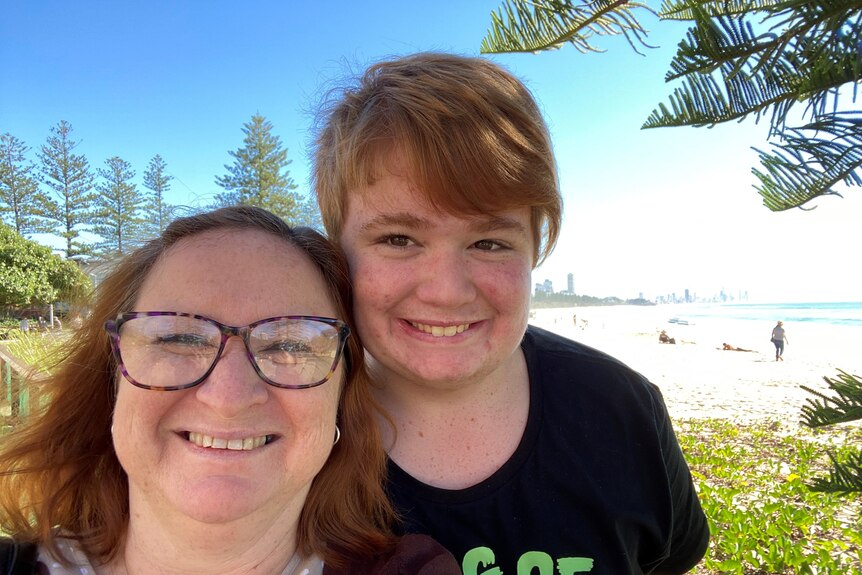 Selfie of a red-haired lady wearing glasses and a teenage boy on a beach