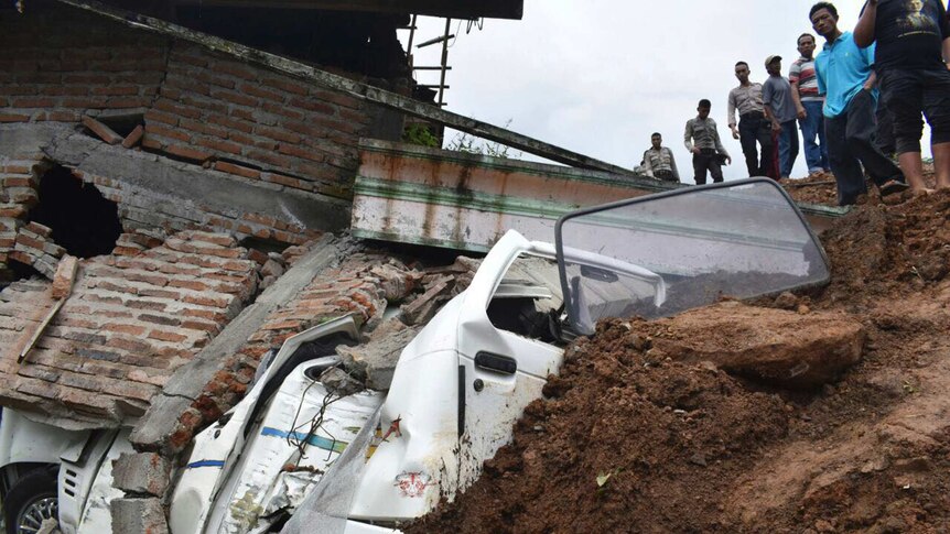 Rescuers gather around a house that fell on a car in Indonesia, following a landslide.