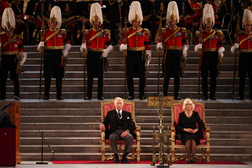 King Charles and Queen Consort Camilla sit on thrones in front of kingsmen.