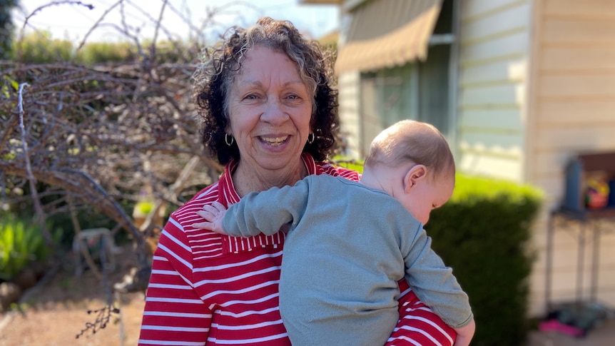 Woman holding an unidentified baby in her front garden. 