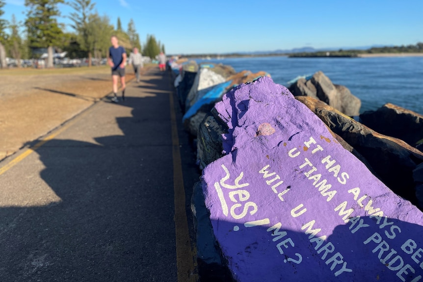 A purple painted rock on a breakwater, with the words 