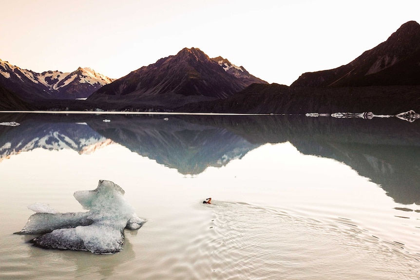 A man swimming past an iceberg.