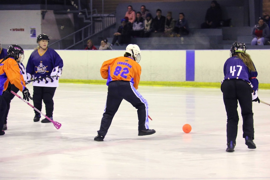 Two teams play broomball on an ice rink.