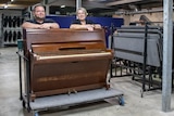 an old upright piano with two people standing smiling behind it