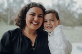 Woman with dark curly hair smiles and hugs her young son