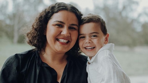 Woman with dark curly hair smiles and hugs her young son