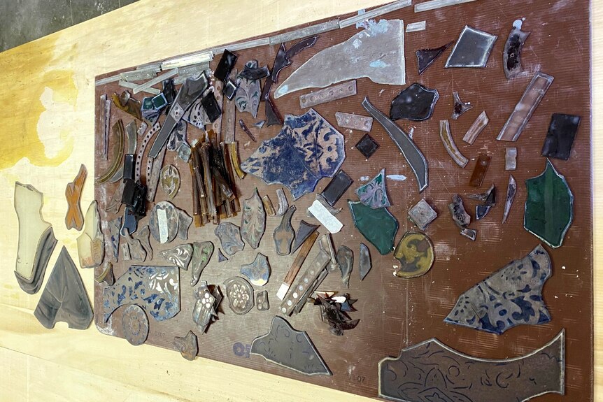 Photograph of a disassembled stained glass window, in bits on a wooden table