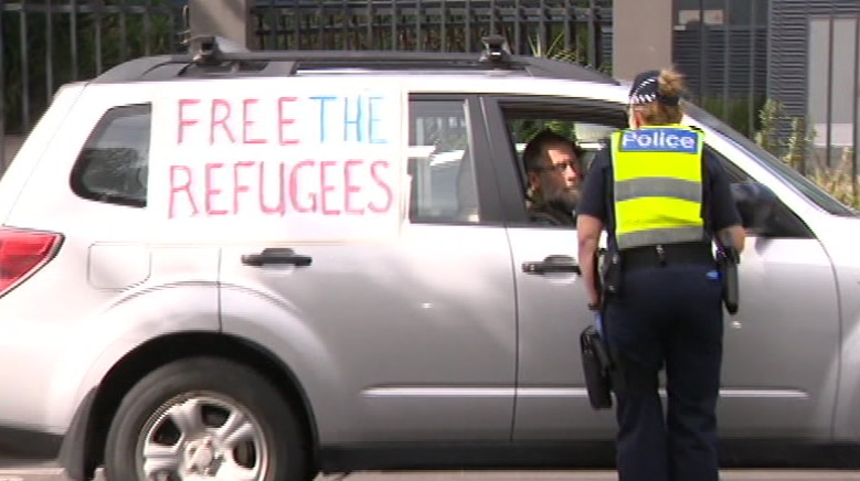 A police officer stands next to a car in a residential street bearing refugee support messages as they issue a fine.