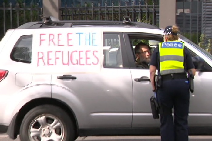 A police officer stands next to a car in a residential street bearing refugee support messages as they issue a fine.