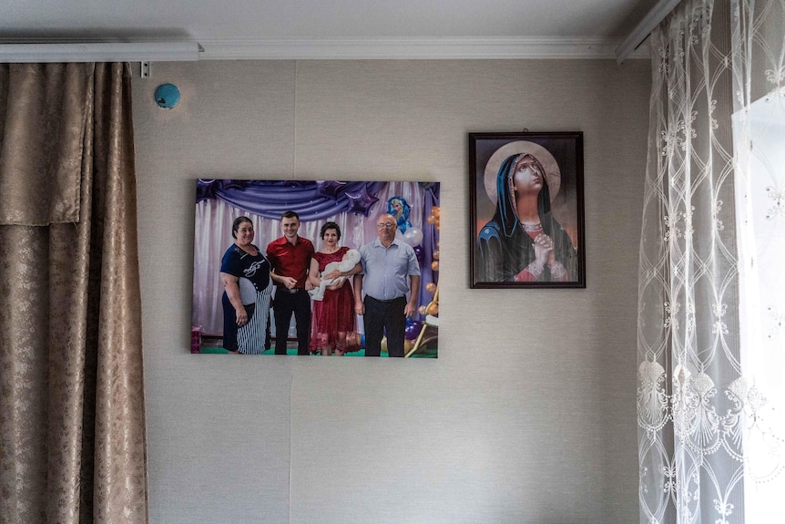 Bronze curtains against a wall with two portraits, one a family photo and the other the Virgin Mary praying. Light peeks in