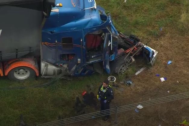 The crushed cabin of a truck with a policeman standing nearby. 