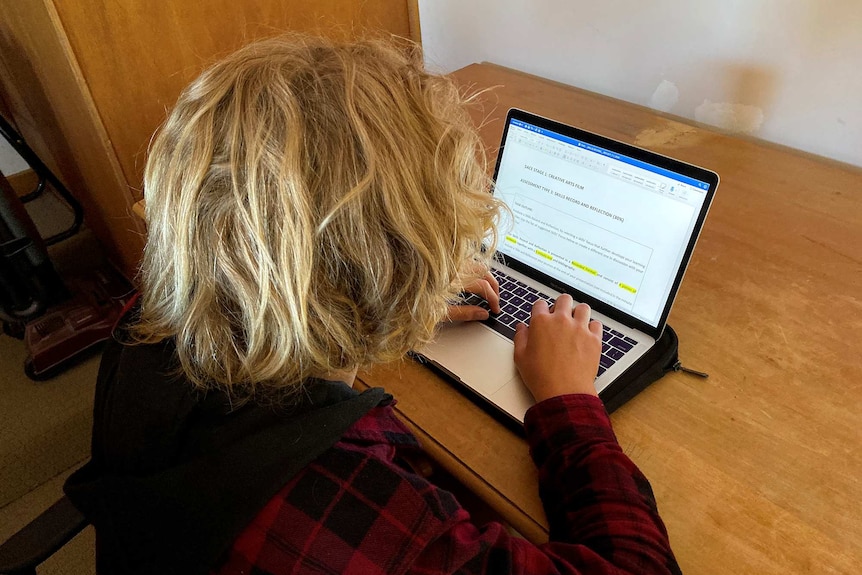 A young student sits in front of a laptop with learning material on the screen.