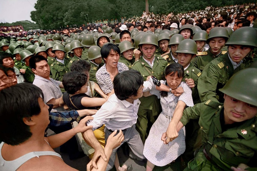 A woman is accosted by Chinese army and protestors as they both grab at her to prevent her from being arrested.