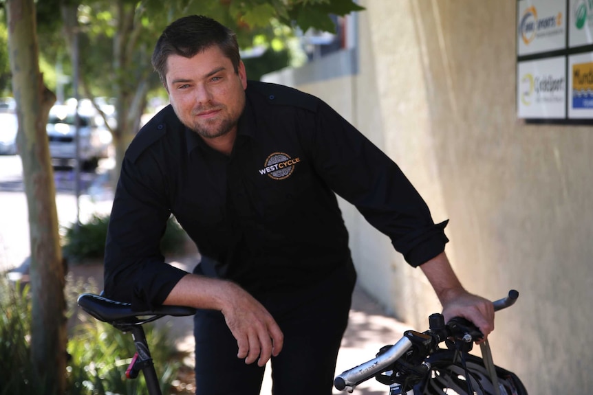 A mid-shot of Westcycle CEO Matt Fulton posing for a photo leaning on a bicycle on a footpath.