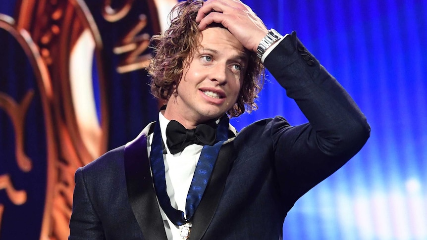Nat Fyfe holds his head with his left hand whilst wearing a black dinner jacket and bow tie with a medal around his neck