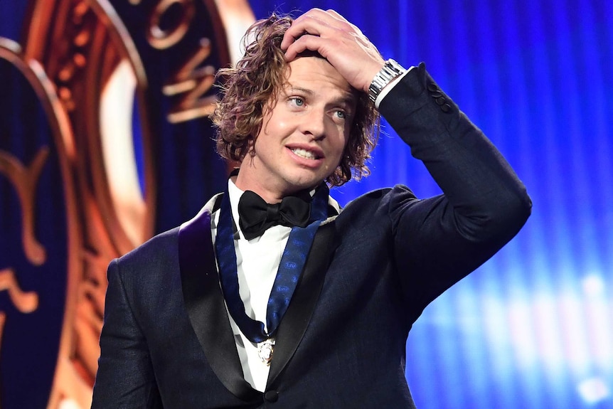 Nat Fyfe holds his head with his left hand whilst wearing a black dinner jacket and bow tie with a medal around his neck