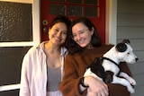 Two young women outside a red front door, smiling and holding a dog, in story about going to friends' places uninvited.