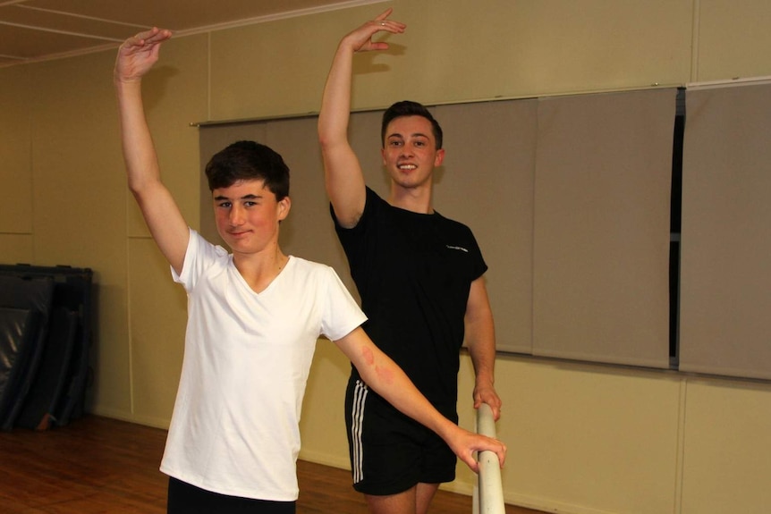 Queensland Ballet teacher Callyn Farrell and student Jack Sullivan stand at barre with arm raised in position.