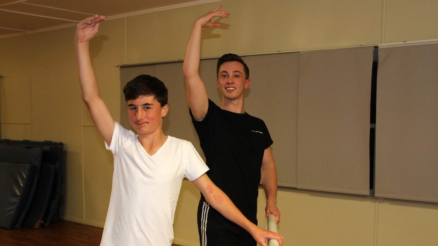 Queensland Ballet teacher Callyn Farrell and student Jack Sullivan stand at barre with arm raised in position.