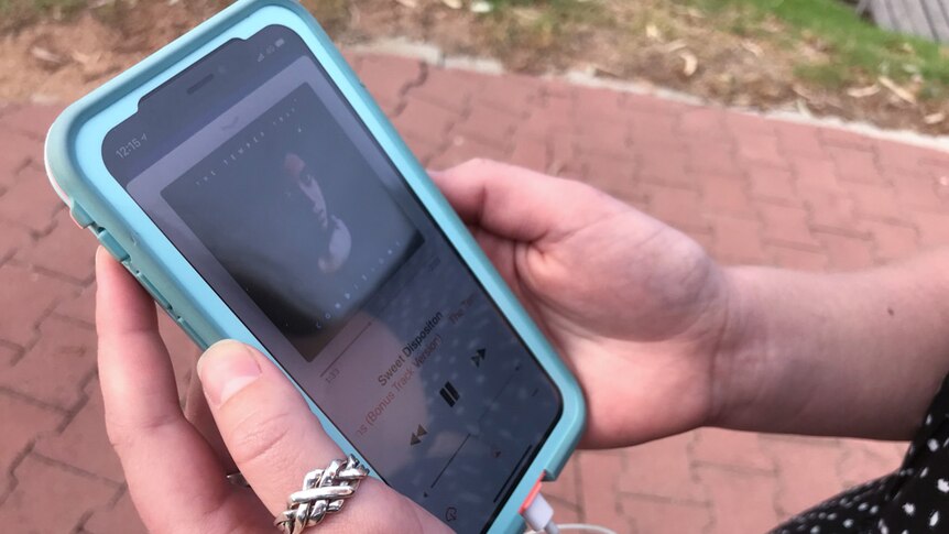 A phone with a track of music playing is held between a young woman's hands.