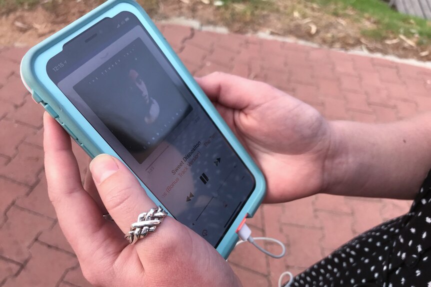 A phone with a track of music playing is held between a young woman's hands.