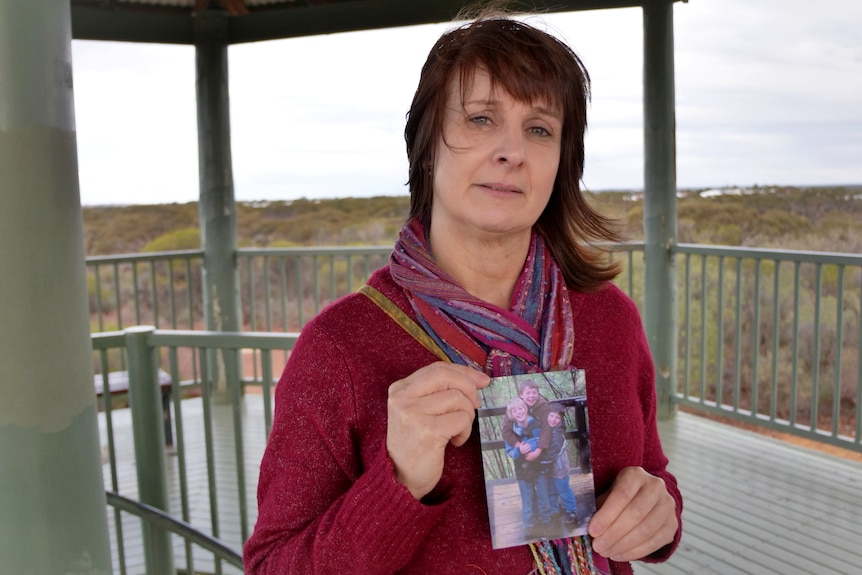 A dark-haired woman holds a picture of her son.