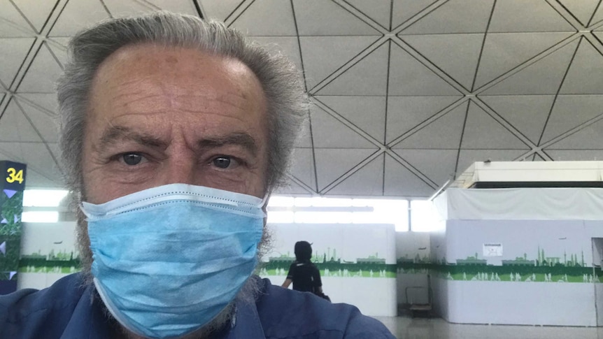 A selfie of Colin wearing a face mask over his mouth sitting in Hong Kong airport- he looks exhausted.