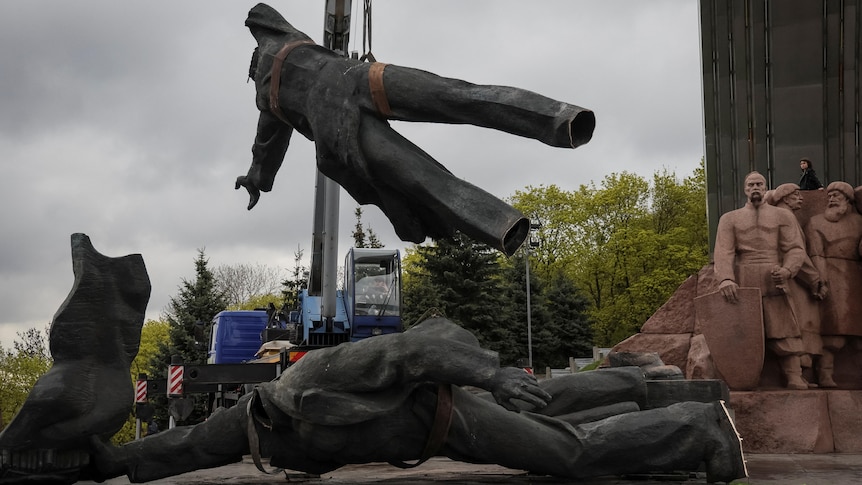 A human shaped bronze statue is dismantles by cranes.