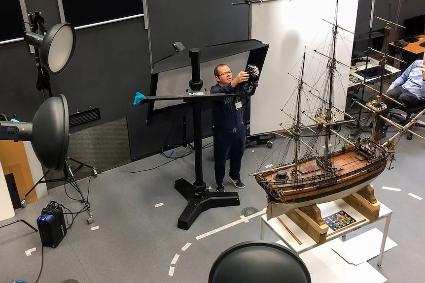 Dr McCarthy is holding a camera taking a scan of a model ship