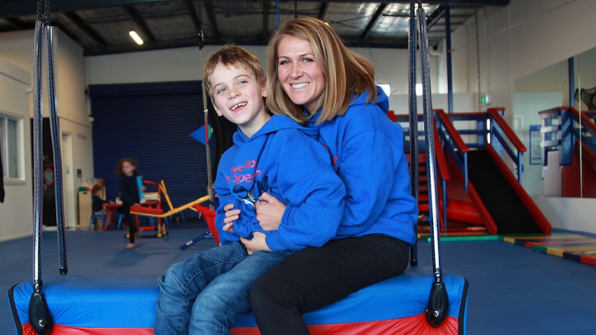 Sally Johnson and her son Digby sit on a swing in the Rock the Spectrum kids play gym.
