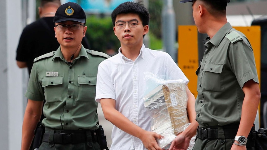 Joshua Wong walks out of prison carrying a stack of books and flanked by two guards.