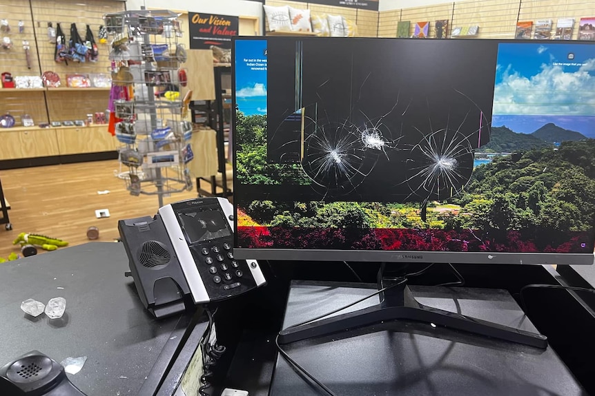 A computer screen with three cracks in it, the centre trashed in the background