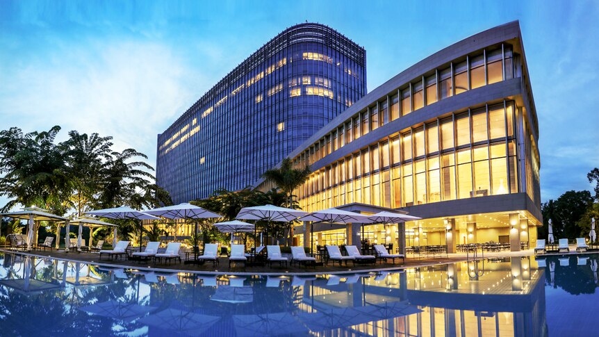 A view of umbrellas by a pool with a large golden-lit building at a hotel.