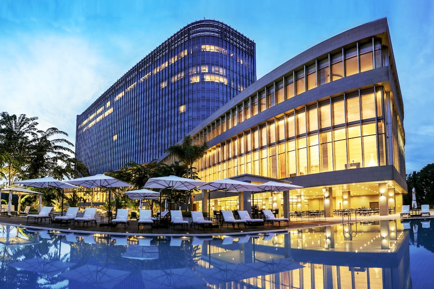 A view of umbrellas by a pool with a large golden-lit building at a hotel.