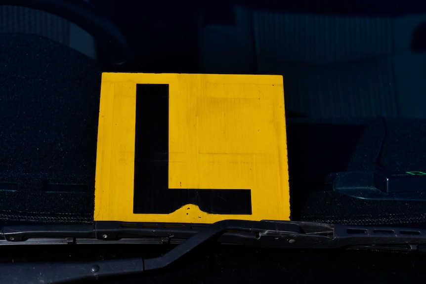 An yellow plate with a black 'L' sitting in the front window of a car. 