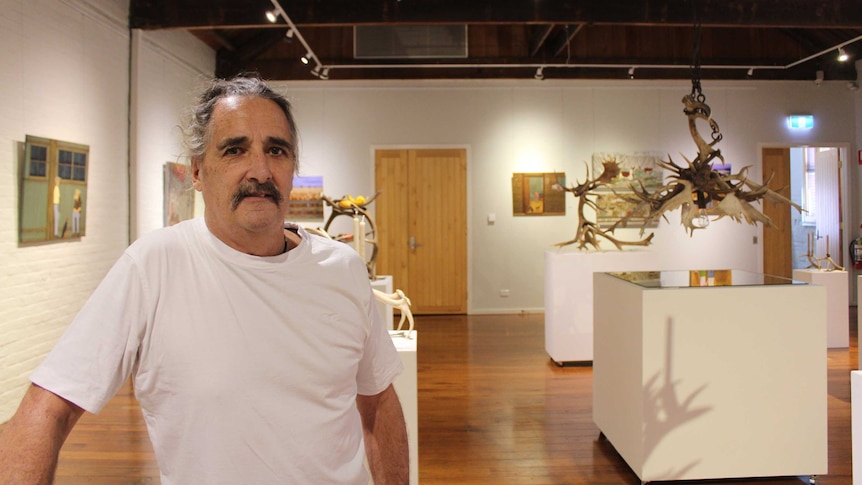 Steve Junghenn stands in a gallery surrounded by his paintings and sculptures
