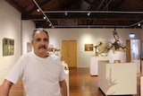 Steve Junghenn stands in a gallery surrounded by his paintings and sculptures