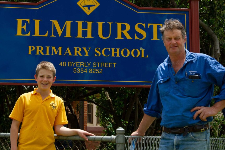 A boy and a man stand in front of an Elmhurst school sign.