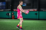 Caleb Neyenhuis in a brightly coloured pink uniform with yellow trims about to kick a football.