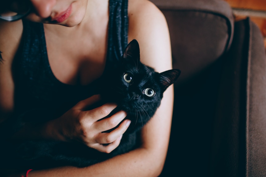 A woman wearing a dark singlet cuddles a black cat